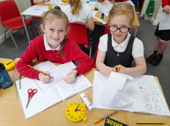 A group of girls sitting at a table with paper and pencils

Description automatically generated