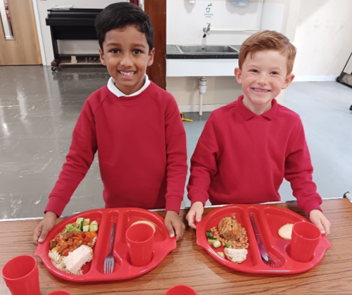 Two boys in red shirts at a table with plates of food

Description automatically generated